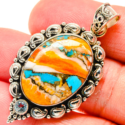 Close-up oval turquoise-orange cabochon pendant in silver filigree with blue topaz-style stones