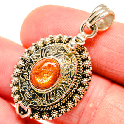 Round filigree pendant with orange sunstone cabochon, silver-tone bail