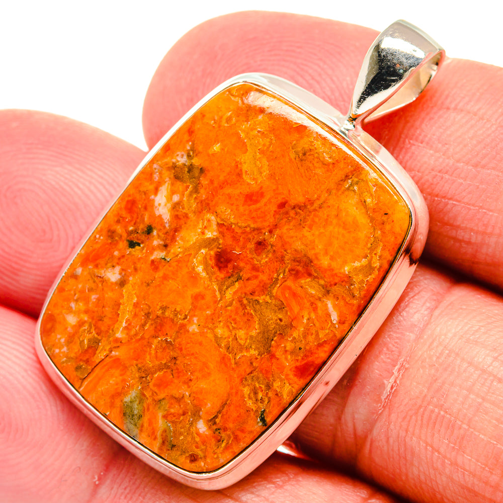 Orange sponge coral pendant in 925 sterling silver bezel, worn on fingertip close-up
