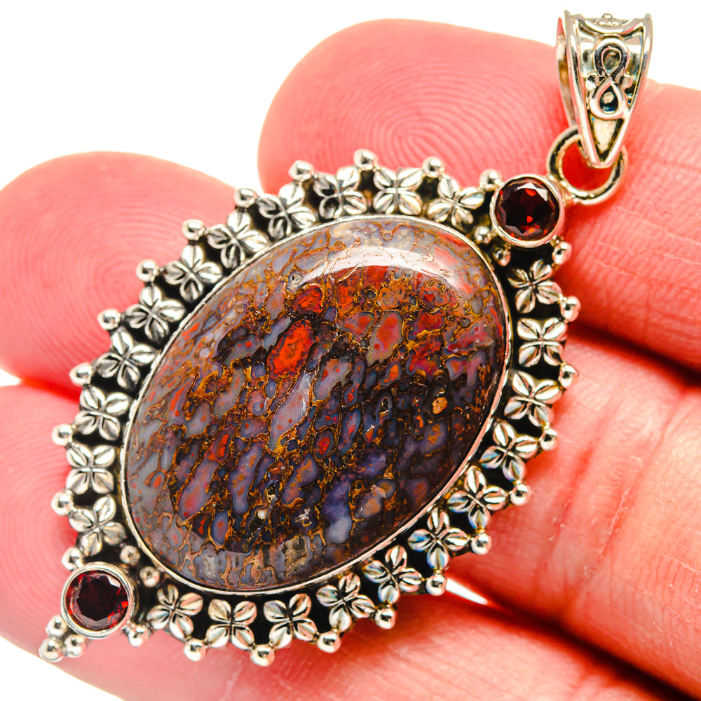 Close-up oval 925 sterling silver pendant with marbled dinosaur-bone pattern and red garnets