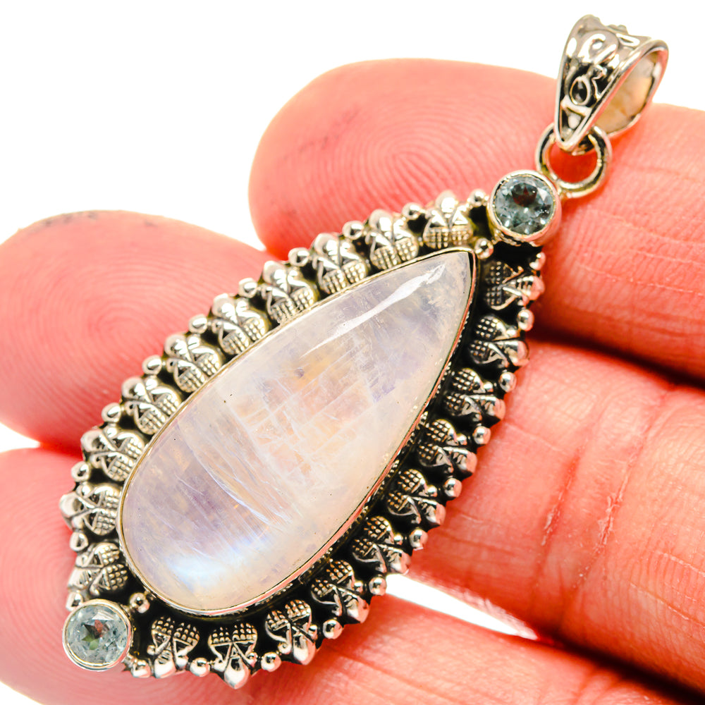 Opalescent teardrop moonstone pendant with ornate silver setting and blue round stones
