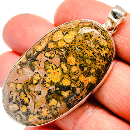 Oval yellow and black pendant stone in silver bezel, shown with hand scale.