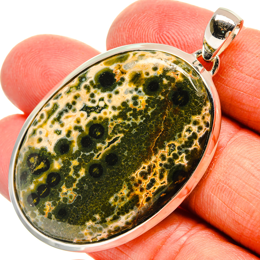 Oval ocean jasper cabochon pendant in sterling silver on fingertip, green and gold