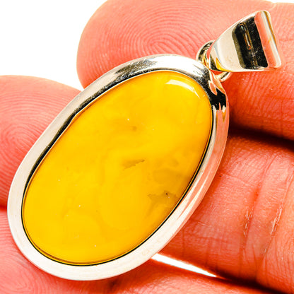 Oval amber pendant in polished silver setting, yellow stone on fingertip