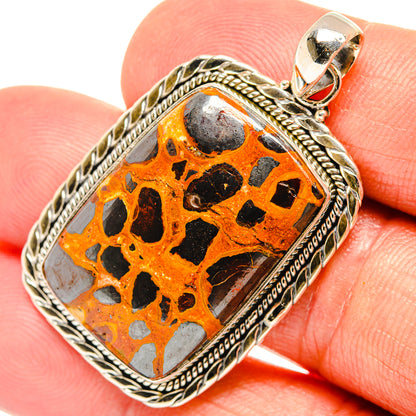 Orange bauxite stone pendant in 925 sterling silver bezel, close-up with black spots