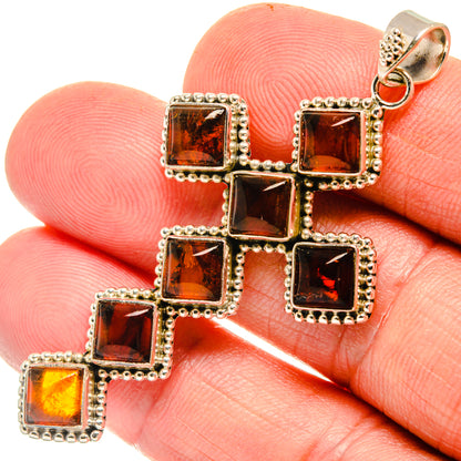 Close-up amber cross pendant with five square dark-orange cabochon stones on silver