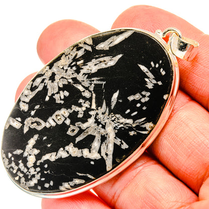 Oval black stone pendant with silver-tone chrysanthemum pattern and metal bail