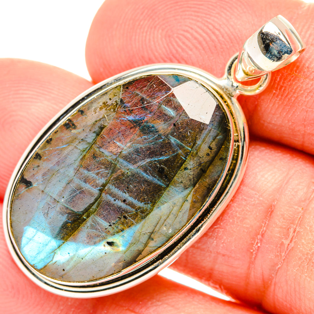 Oval labradorite pendant with stone facets in silver bezel, on a finger