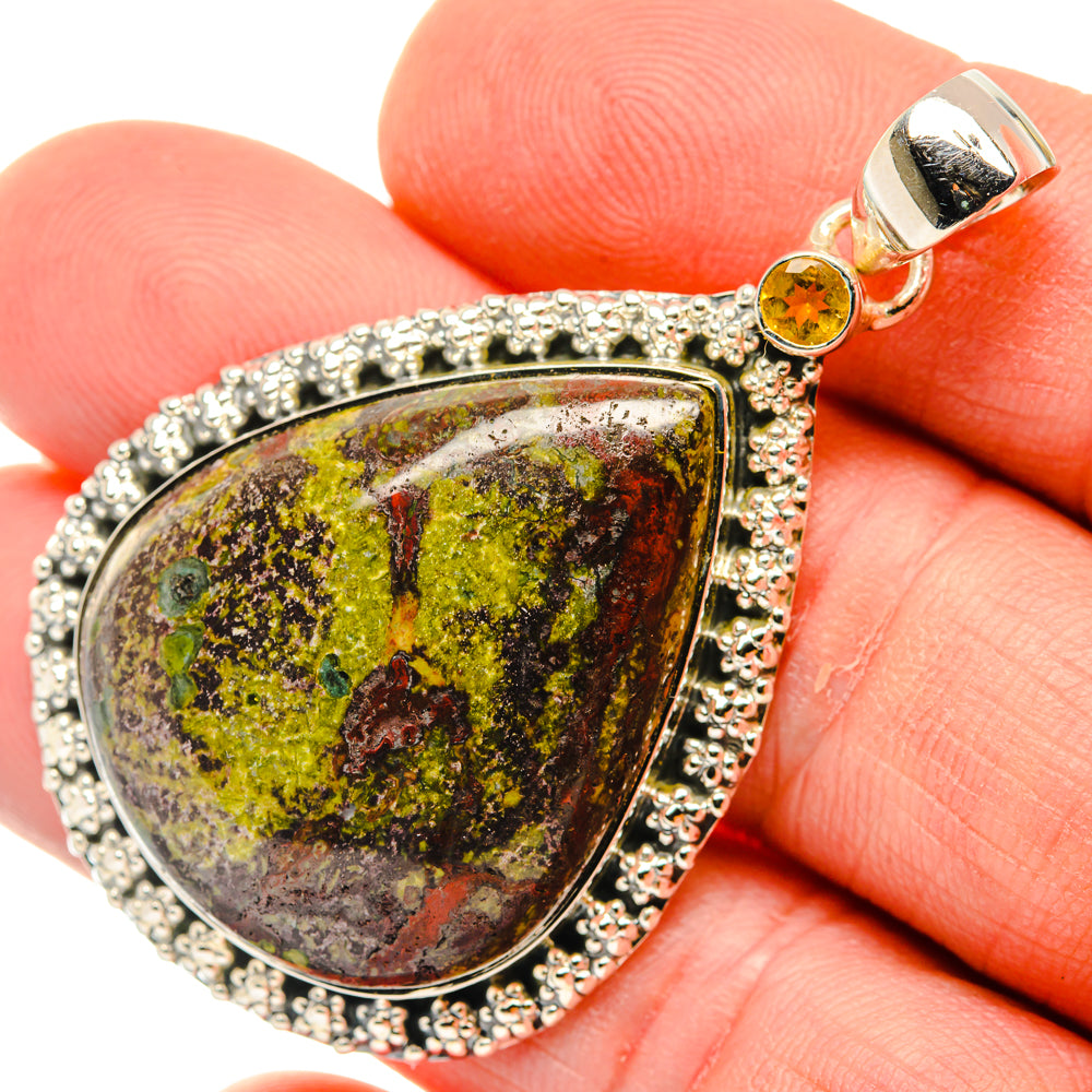 Teardrop gemstone pendant close-up: silver frame, orange round bail, mottled red-green stone