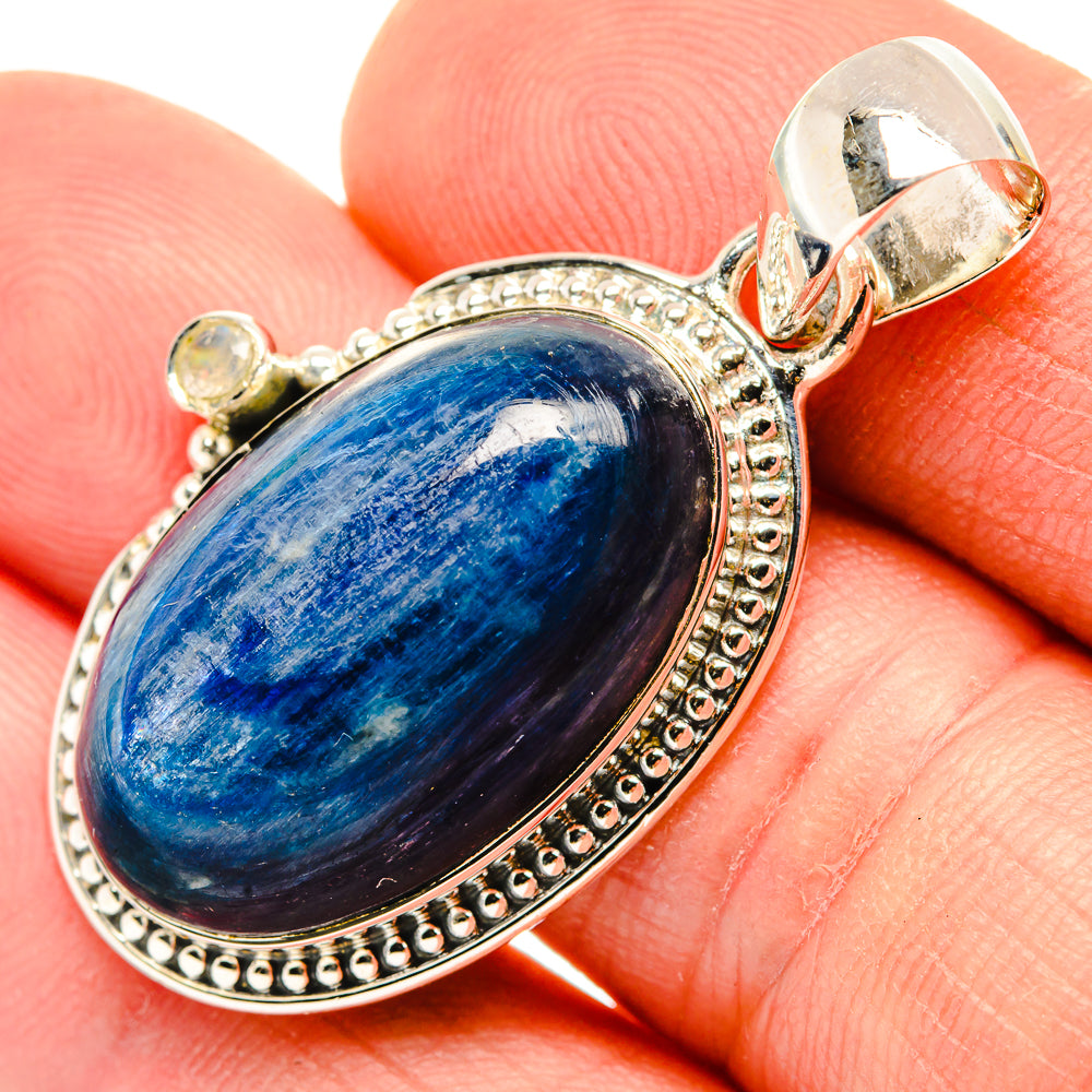 Oval blue stone pendant with beaded sterling silver bezel and bail on finger