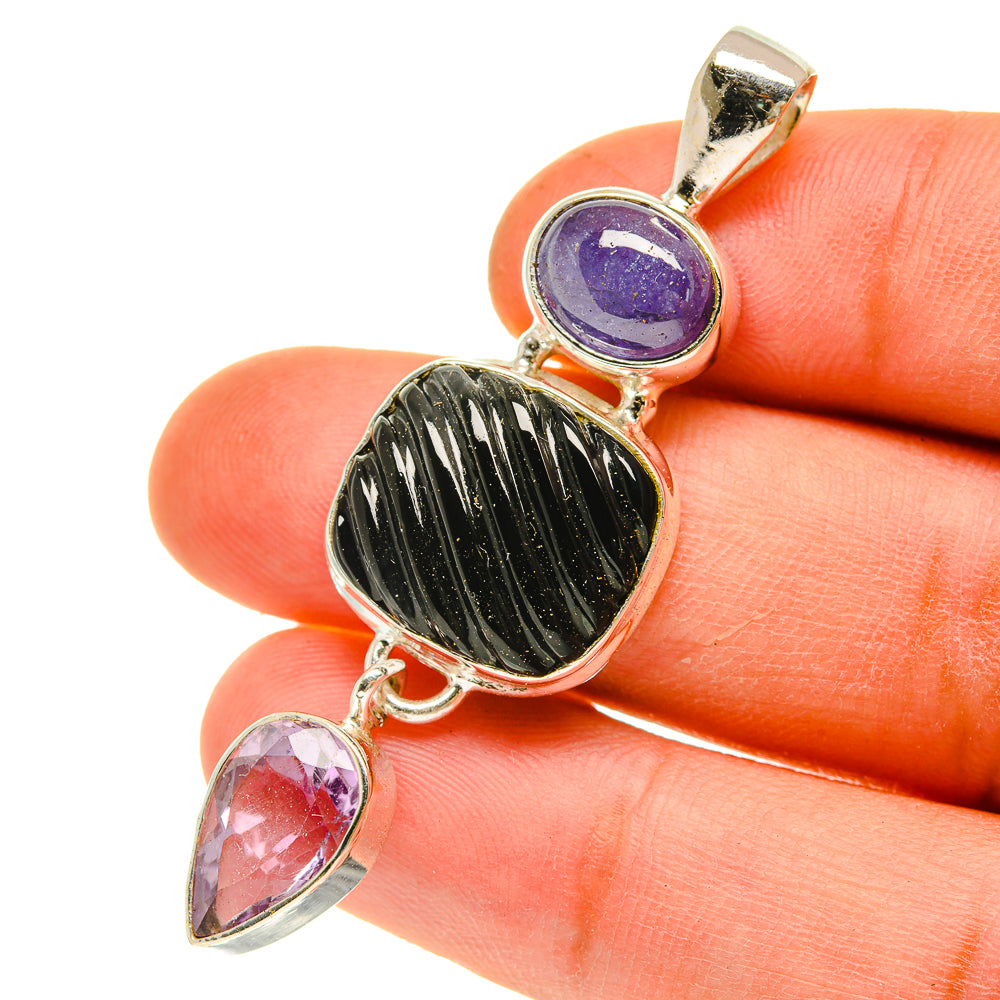 Sterling silver pendant held in hand with purple round stone, black oval stone, and pink teardrops