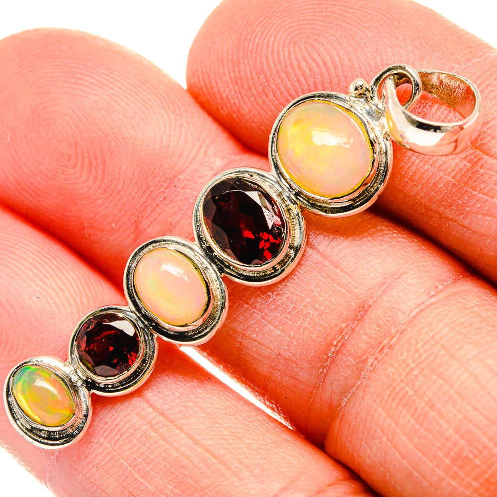 Round opal and red garnet cabochon pendant in sterling silver, close-up on finger