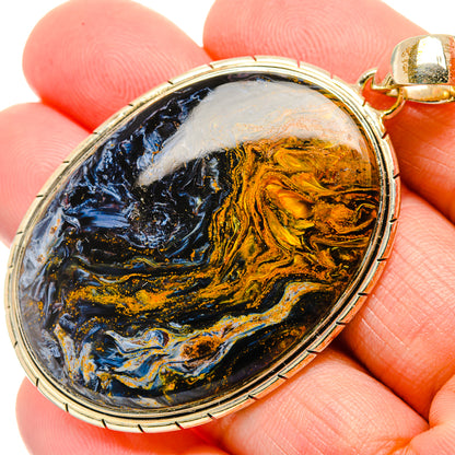 Oval pietersite pendant with blue, black, and gold stone; metal bezel and bail