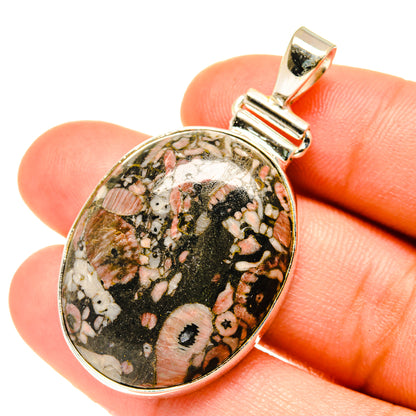 Oval sterling silver fossil pendant with speckled black, pink, and white cabochon stone.
