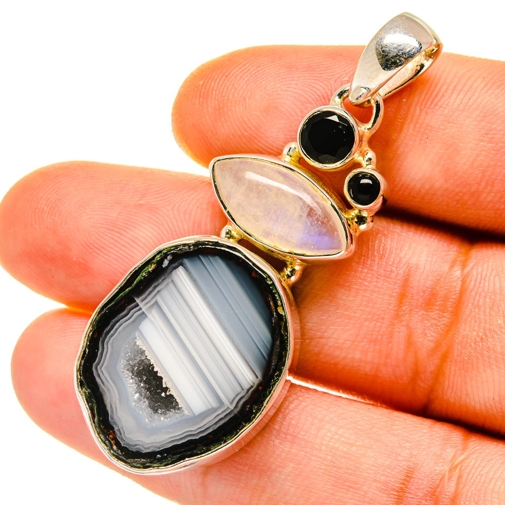 Gold-tone gemstone pendant close-up with oval agate slice, black round stones, and light iridescent
