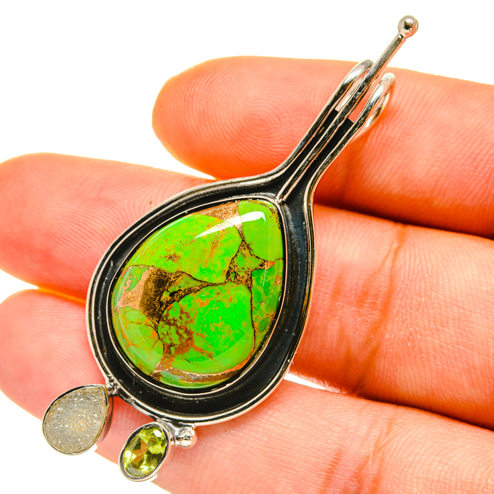 Green stone teardrop pendant close-up with black border, gold-tone charm and peridot-colored drop.