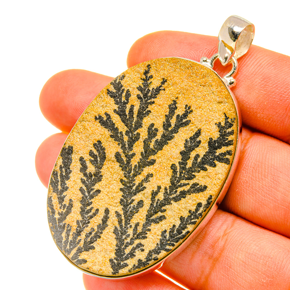 Oval psilomelane dendrite pendant, yellow with black branching pattern, held in hand