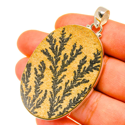 Oval psilomelane dendrite pendant, yellow with black branching pattern, held in hand