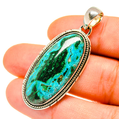 Oval green-and-turquoise stone pendant in silver bezel, held between fingers