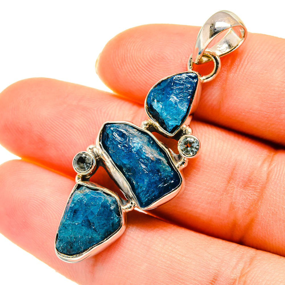 Blue gemstone pendant shown with small round clear stones in a gold-tone frame