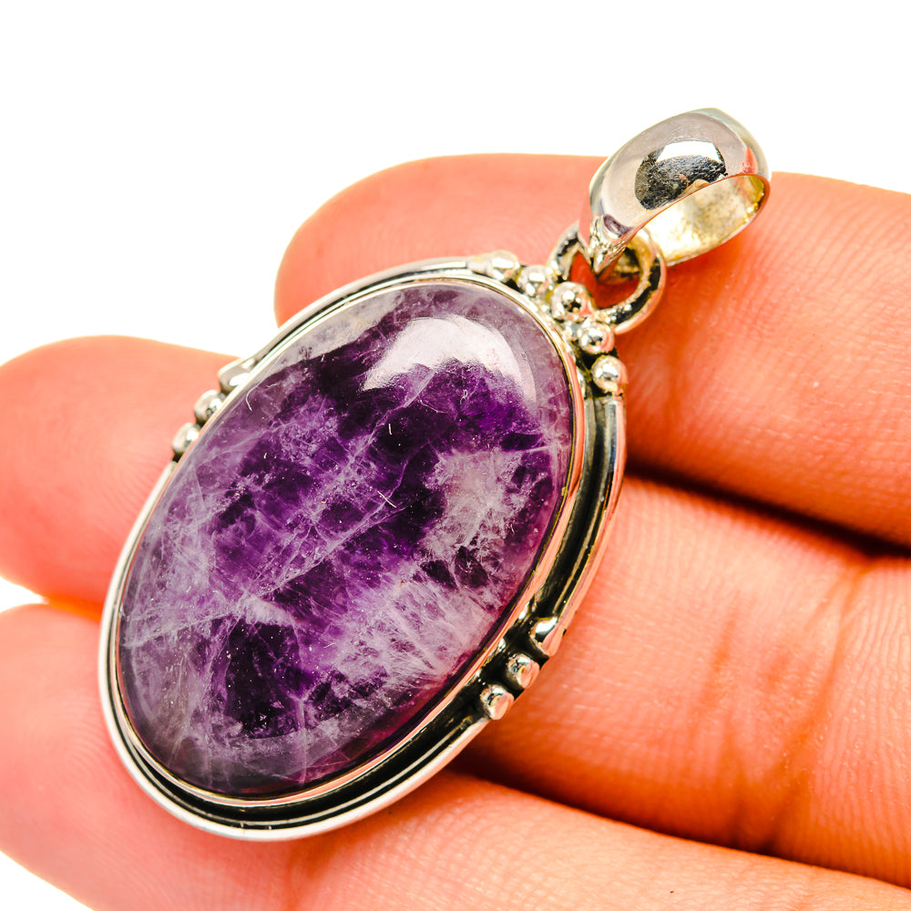 Oval amethyst cabochon pendant with sterling silver bail, held in hand