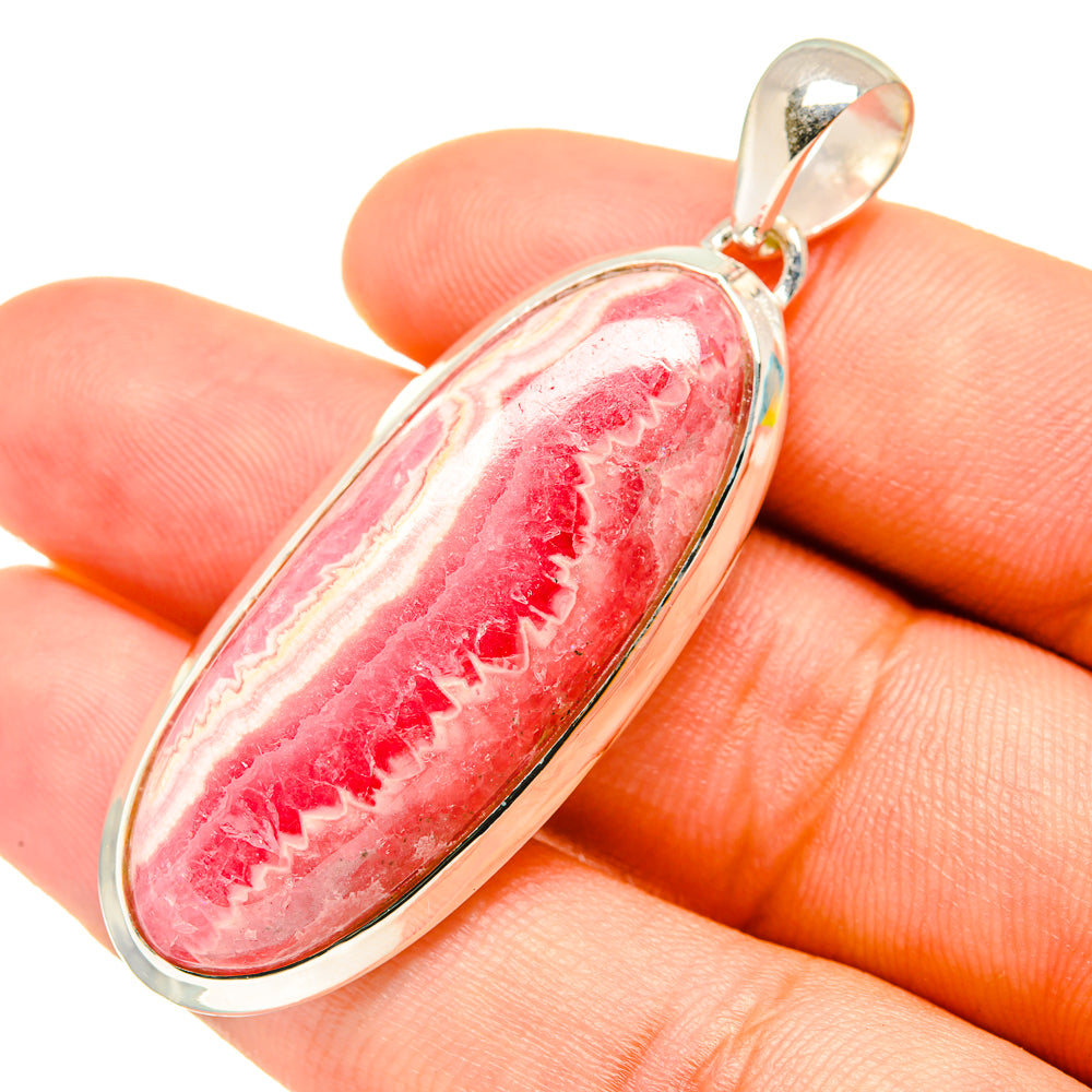 Oval pink rhodochrosite cabochon pendant in sterling silver bezel, shown held in hand