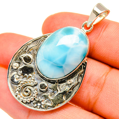Larimar oval pendant with ornate silver frame, shown on hand