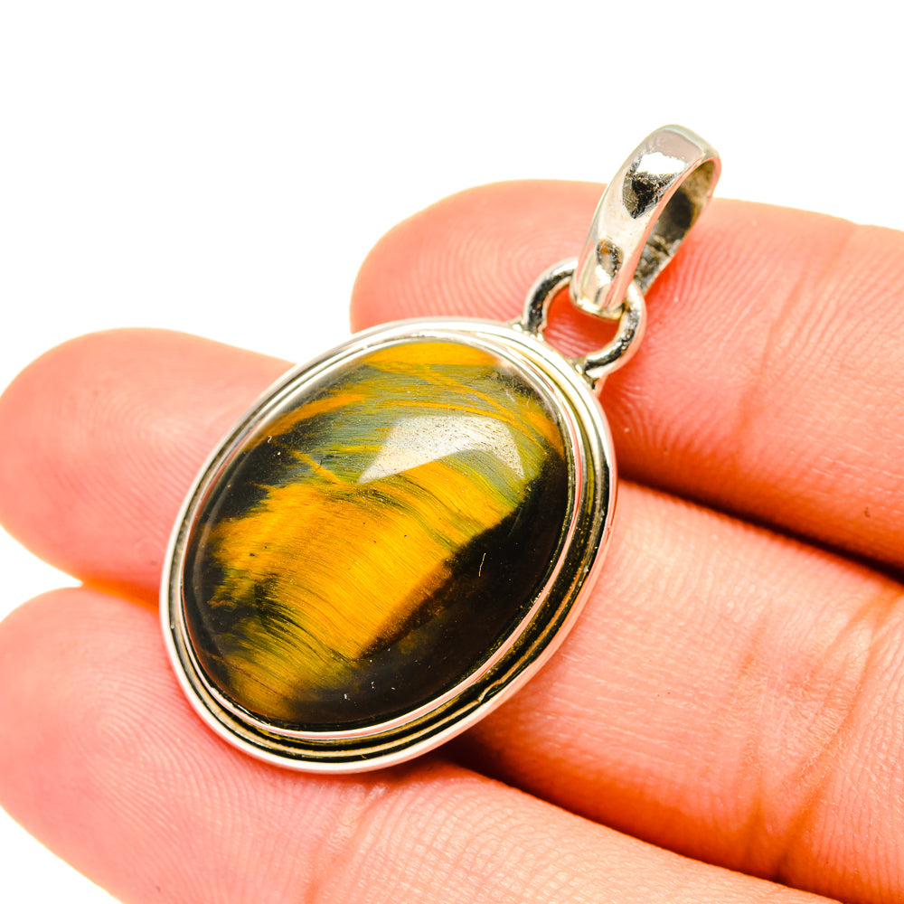 Tiger eye pendant close-up on finger: oval silver bezel and gold-toned bail