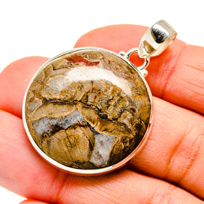 Round silver-framed mushroom rhyolite pendant on fingertip, mottled gold, white, and dark