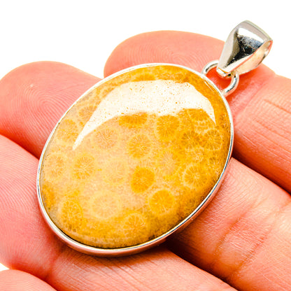 Oval orange coral pendant with silver bezel on close-up hand