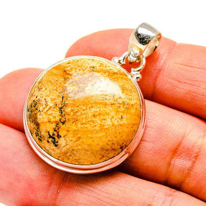 Sterling silver pendant with round picture jasper stone on orange fingertips, side view.