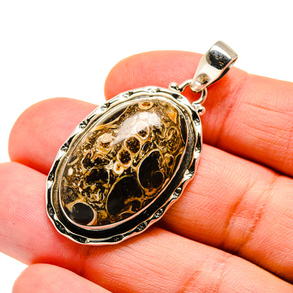 Sterling silver oval agate pendant with dark amber fossil stone, shown on finger