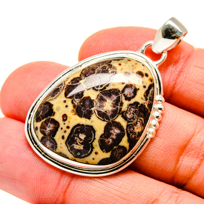 Oval sterling silver pendant with poppy jasper cabochon, held on fingertip