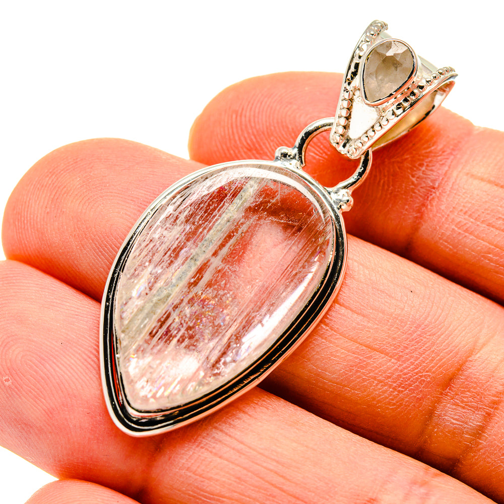 Oval rainbow moonstone pendant, ornate silver setting, shown on fingers