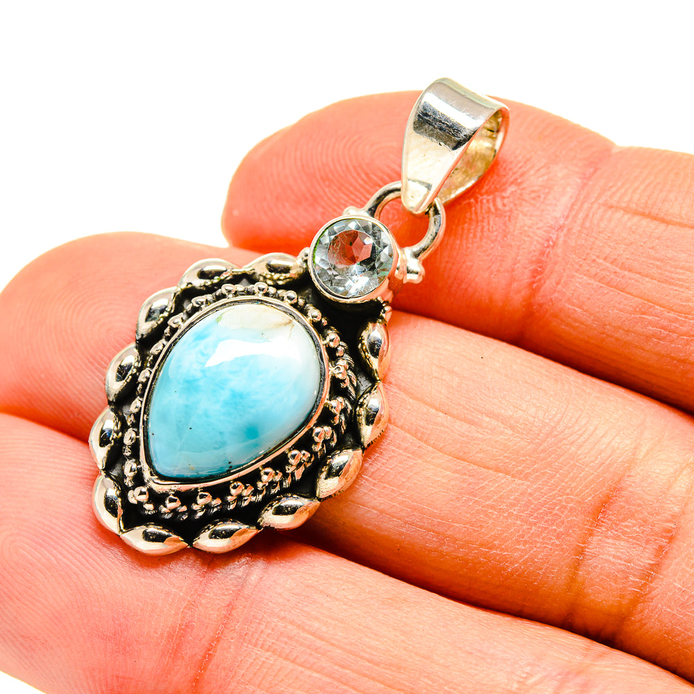 Round blue gemstone pendant with ornate silver-tone bezel and small clear accent stone