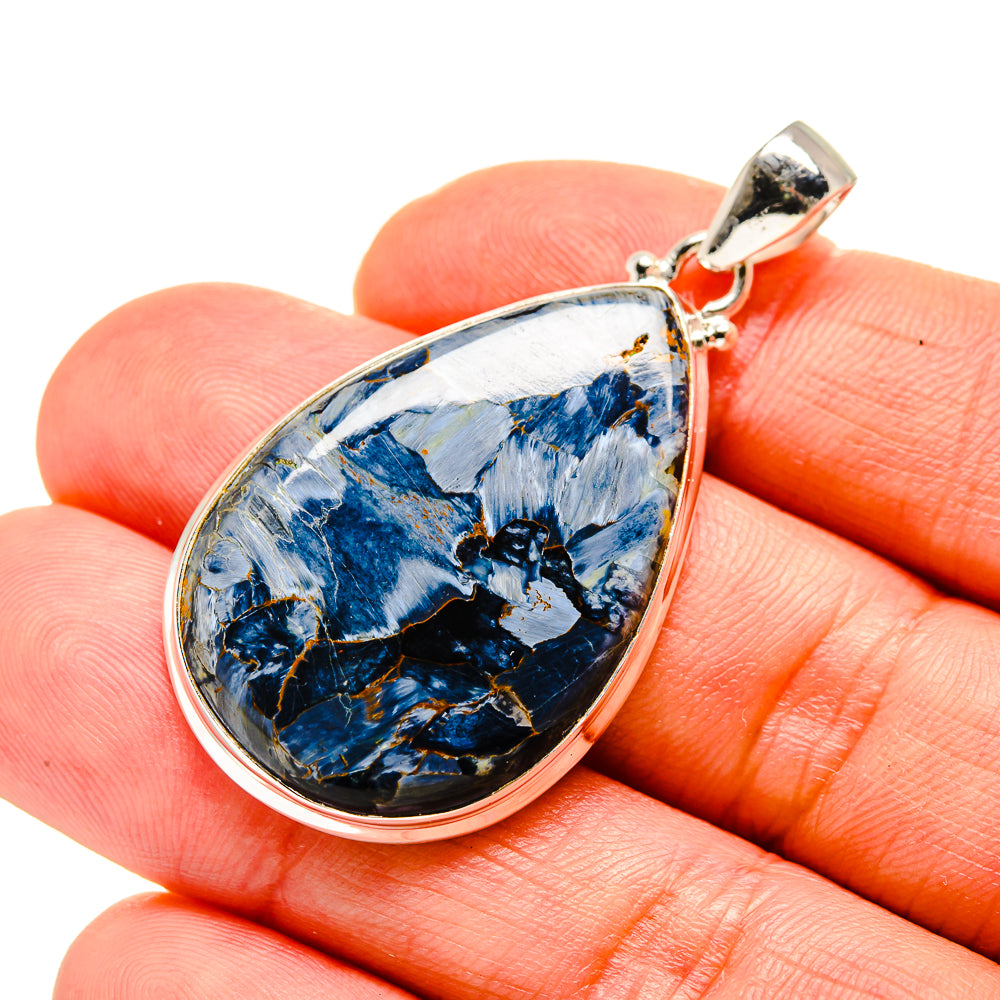 Teardrop pietersite pendant with silver bail over blue veined stone, held in fingers