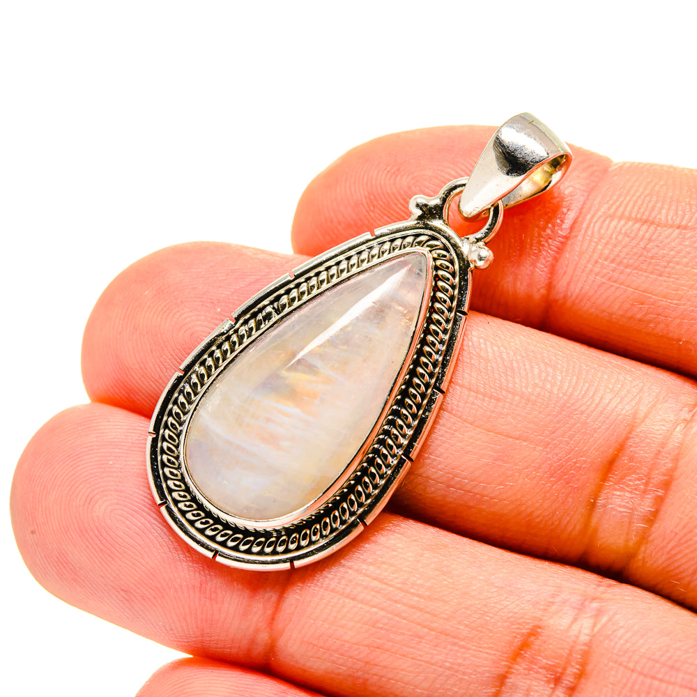 Opalescent oval moonstone pendant in ornate silver bezel with bail, close-up on finger