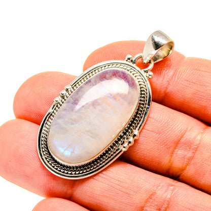 Oval moonstone pendant in silver setting held in fingertips