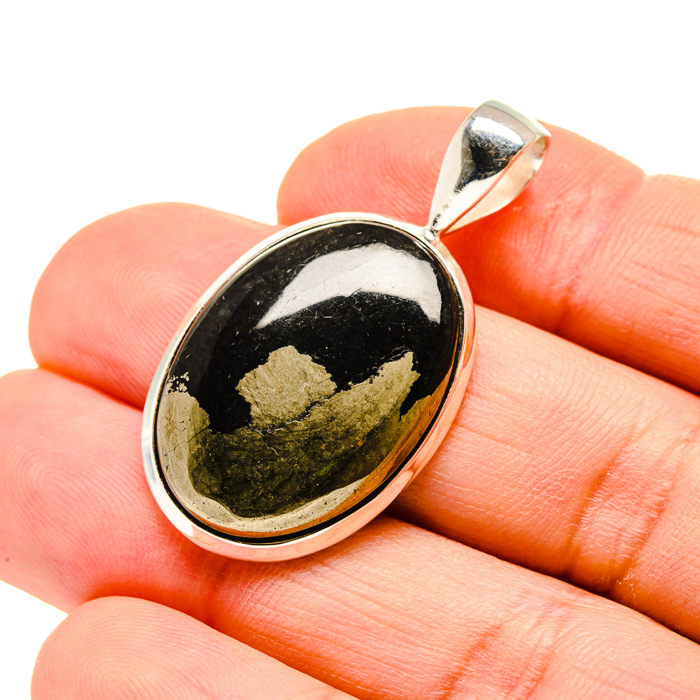 Oval black gemstone pendant, sterling silver bezel with gold flecks, shown on hand