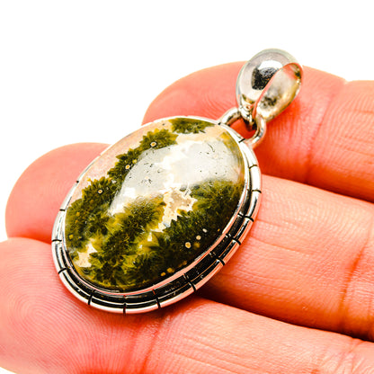 Oval jasper pendant held in hand, green and gold speckled cabochon with silver bezel