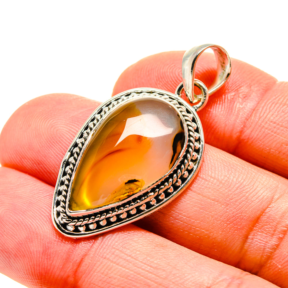 Orange and gold teardrop agate pendant with engraved silver-tone 925 bail on finger