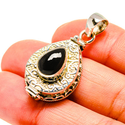Black onyx teardrop pendant with ornate filigree frame, on finger