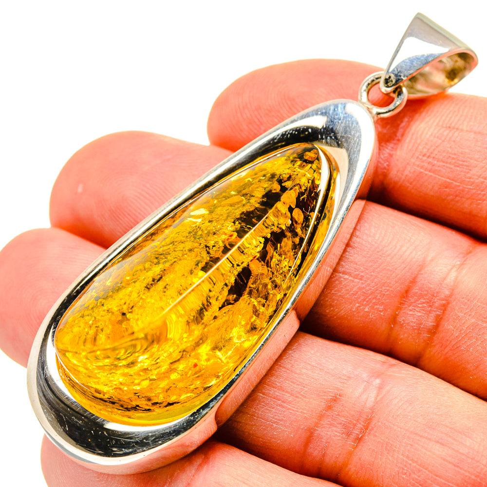 Silver-framed teardrop Baltic amber pendant with gold bail, on finger
