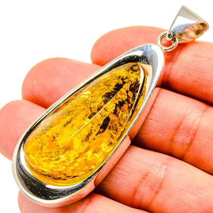 Silver-framed teardrop Baltic amber pendant with gold bail, on finger