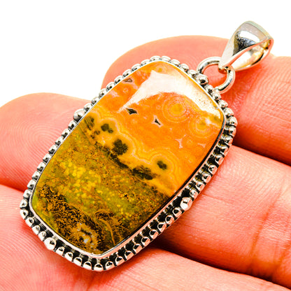 Rectangular orange-yellow jasper pendant on finger, silver bezel and bail