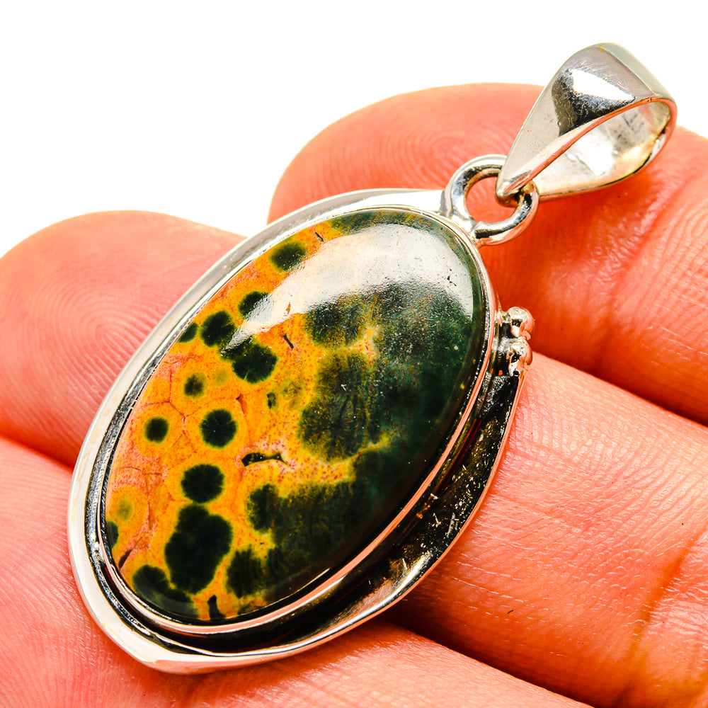 Oval ocean jasper pendant in 925 sterling silver on finger, orange and dark green mottled cabochon