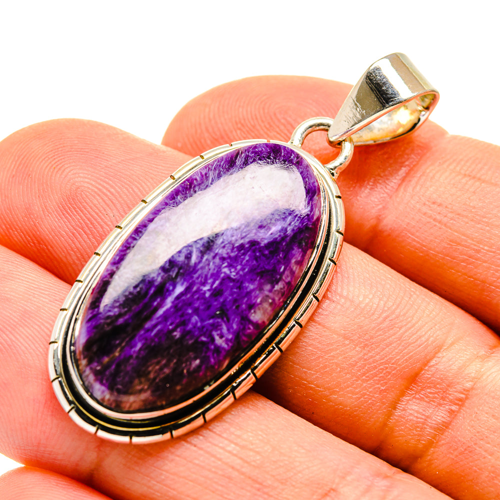 Oval purple charoite pendant with sterling silver frame and gold-tone bail, close-up.