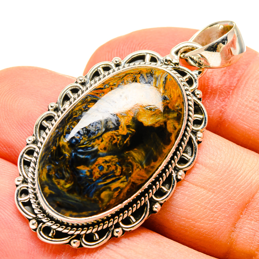 Pietersite pendant oval stone with blue and gold swirls, silver setting, on finger