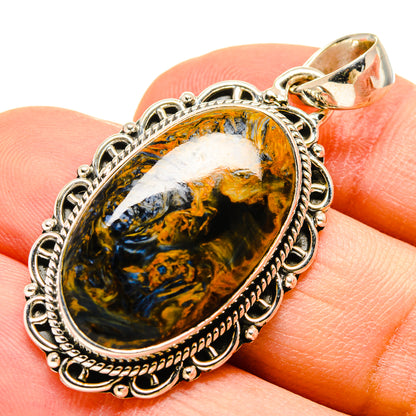 Pietersite pendant oval stone with blue and gold swirls, silver setting, on finger
