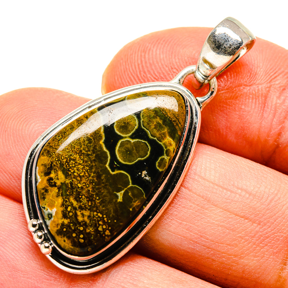 Oval ocean jasper pendant close-up on stone, silver frame with gold-green pattern, bail